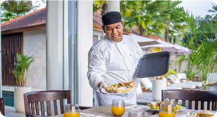 Hotel chef serving a plated breakfast on an outdoor terrace with juice on the table.