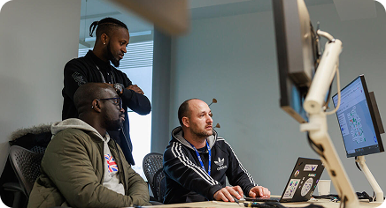 Three teammates collaborating at a desk, gathered around a computer screen in an office.